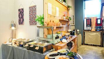 A buffet setup with various food stations, a coffee machine, and a refrigerator in a room with a wooden counter and wall decorations.