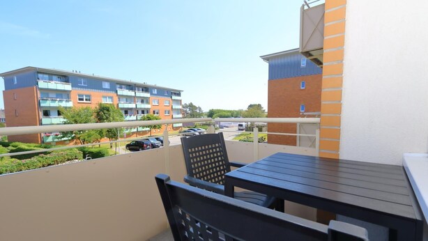 A balcony with a table and chairs, overlooking a parking area and buildings. - Tanja Hüs - in the south grove (Sylt)