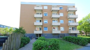 A multi-story apartment building with balconies, a paved entrance, and surrounding greenery. - Tanja Hüs - in the south grove (Sylt)