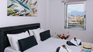 Habitación de hotel con cama, un cuadro, ventana con vista a la ciudad y un jarrón con flores.
