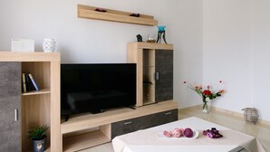 Una sala de estar moderna con un televisor de pantalla plana, mueble de entretenimiento de madera y un comedor con mesa preparada para dos.