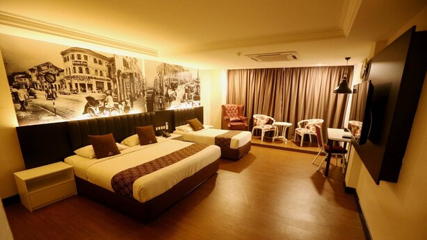 A hotel room with a large bed, a smaller bed, a desk, a chair, a television, and a mural on the wall. - Golden Nasmir Hotel (Perai)