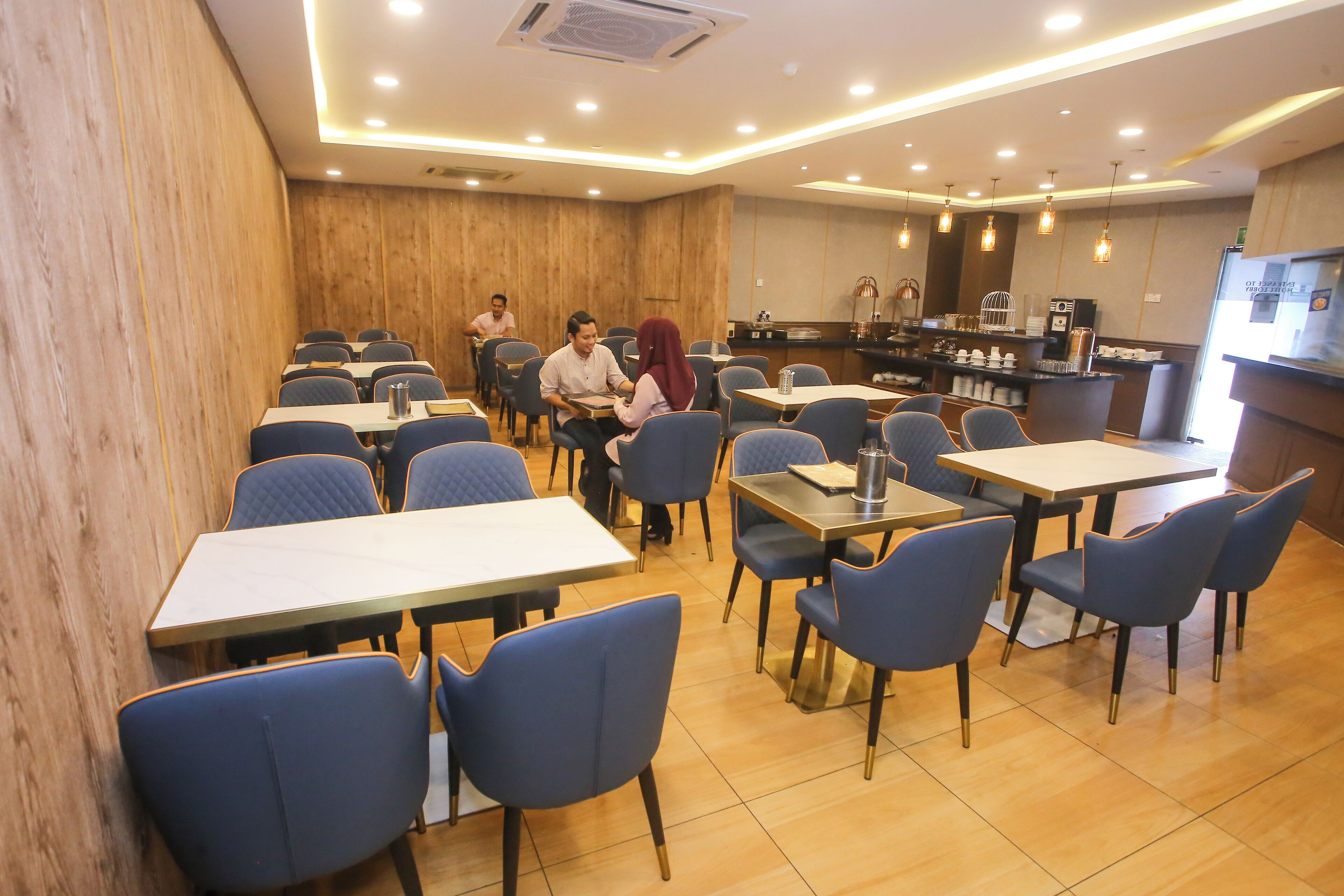 A hotel dining area with multiple tables and chairs, a reception desk, and a coffee station.