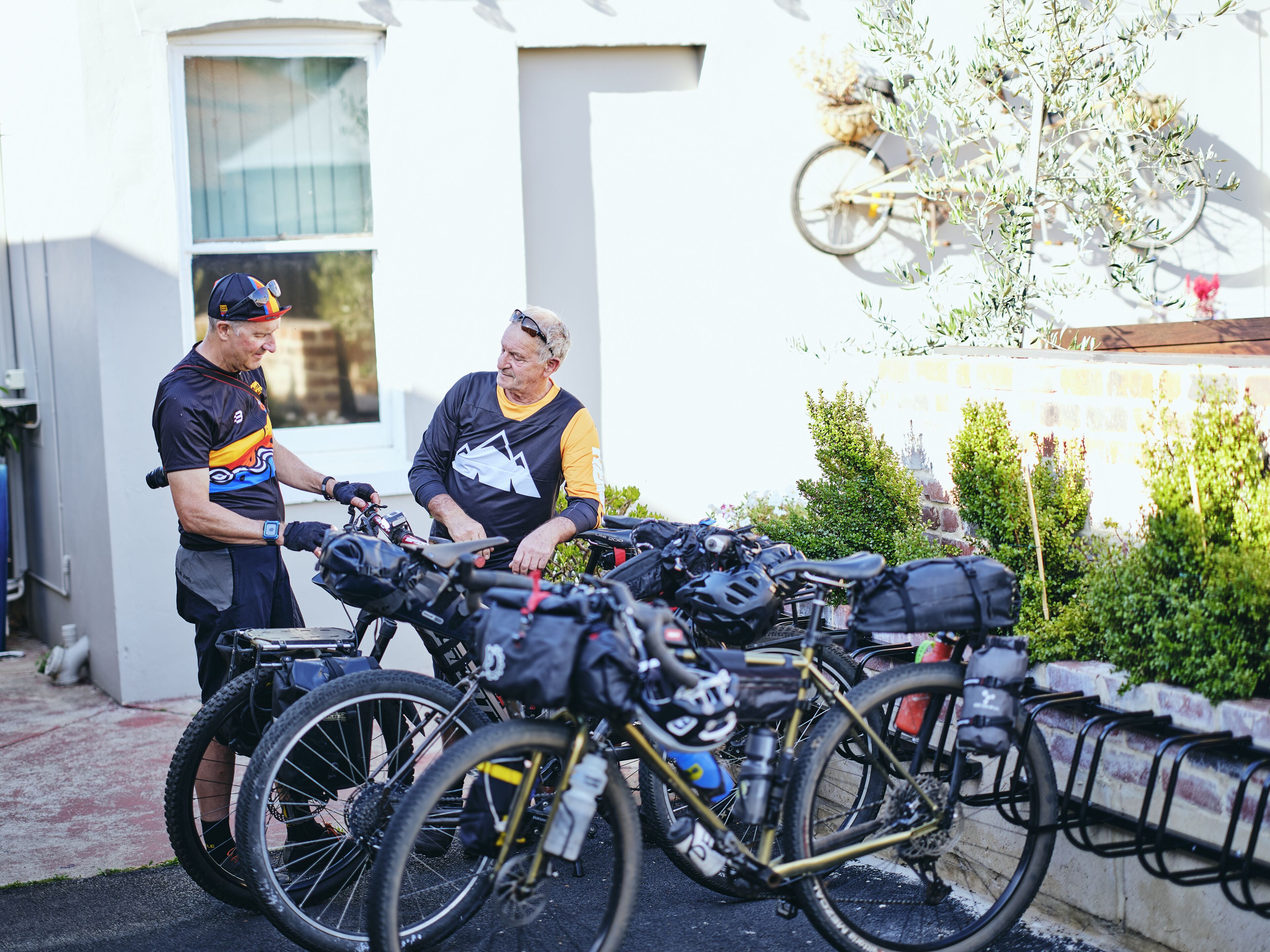 A group of bicycles parked outdoors, possibly in a residential area with a white building in the background.