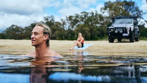 A man in a swimming hole with a vehicle and a person on a beach in the background. - Black Diamond Lodge (Collie)