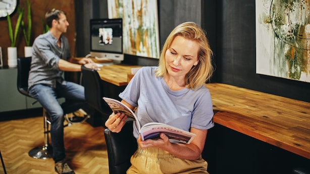 A woman reading a magazine in a modern waiting area with wooden flooring and artwork on the walls. - Black Diamond Lodge (Collie)