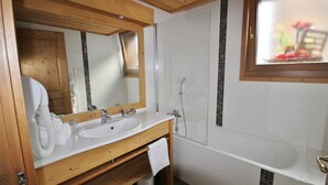 A bathroom with a wooden vanity, a large mirror, a white sink, and a bathtub. - <<<<>>>> (Les Gets)