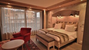 A bedroom with a large bed, a red armchair, a small round table, and a patterned rug. - <<<<>>>> (Les Gets)