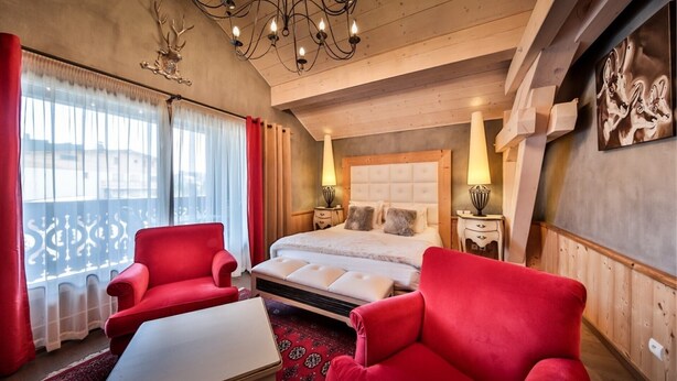 A bedroom with a large bed, two red armchairs, a white coffee table, and a chandelier. - <<<<>>>> (Les Gets)