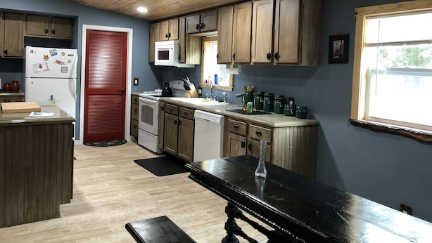 Une cuisine avec des meubles de rangement en bois, une porte rouge, un four à micro-ondes et un évier.