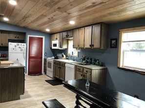 Una cocina con armarios de madera, una puerta roja, un microondas y un fregadero.