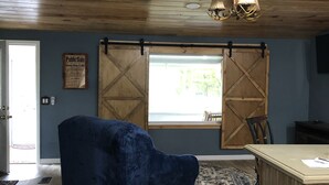 Une pièce avec un plafond en bois, un fauteuil en velours bleu, une table en bois et une fenêtre donnant sur un paysage verdoyant.