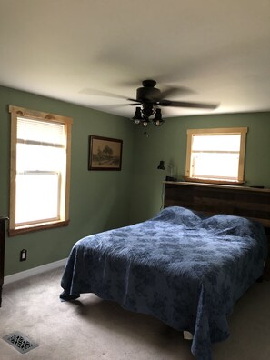 A bedroom with a bed, two windows, a ceiling fan, and a dresser. - Peaceful forest cottage meticulously updated for your comfort. (Ocklawaha)