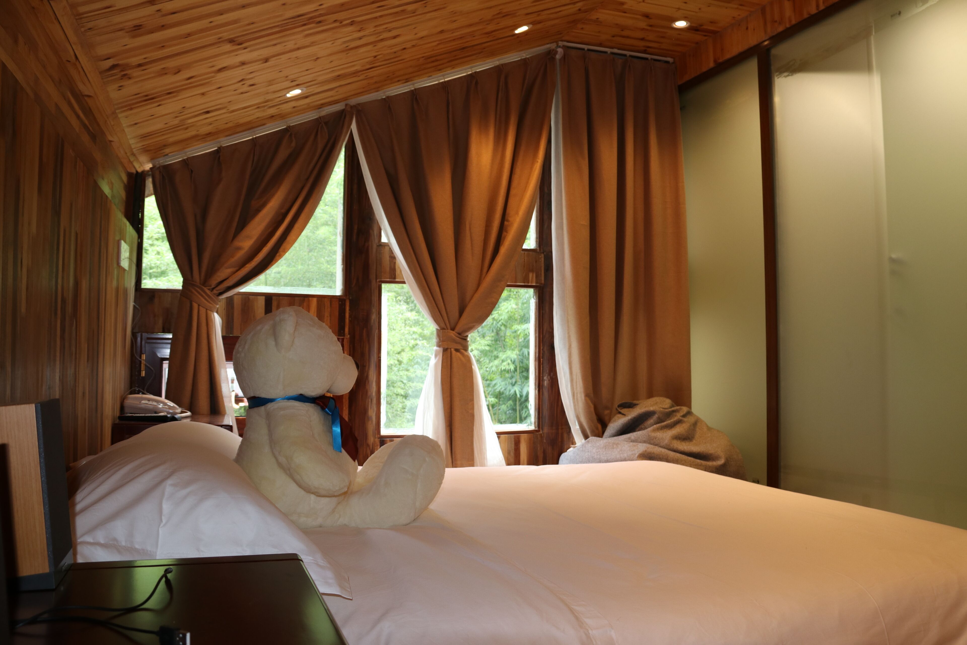 A wooden-paneled room with a bed, a large plush toy, and a laptop on a desk.