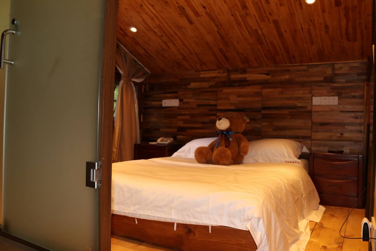 A bedroom with a wooden headboard, a bed with white bedding, a nightstand with a lamp, and a teddy bear on the bed.