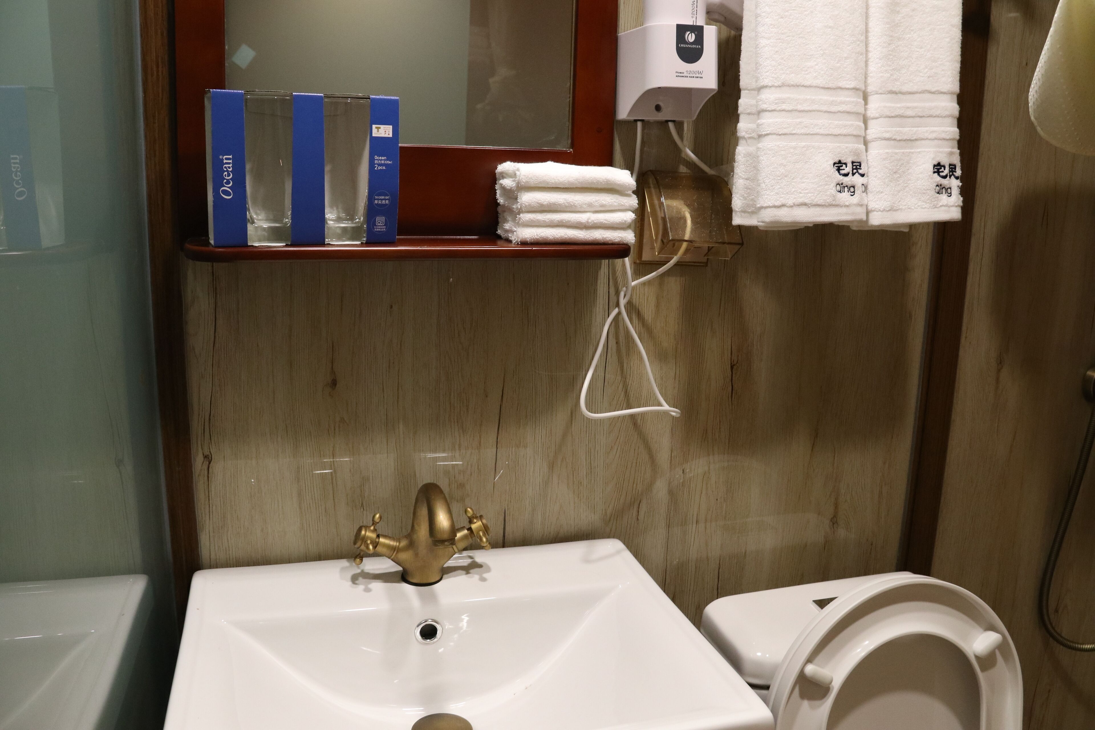 A bathroom with a sink, a mirror, a towel dispenser, and a shelf with toiletries.