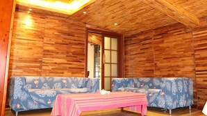 A room with wooden walls and ceiling, two sofas with floral upholstery, a table with a striped tablecloth, and a traditional Japanese sliding door. - Qing Dynasty House (Leshan)