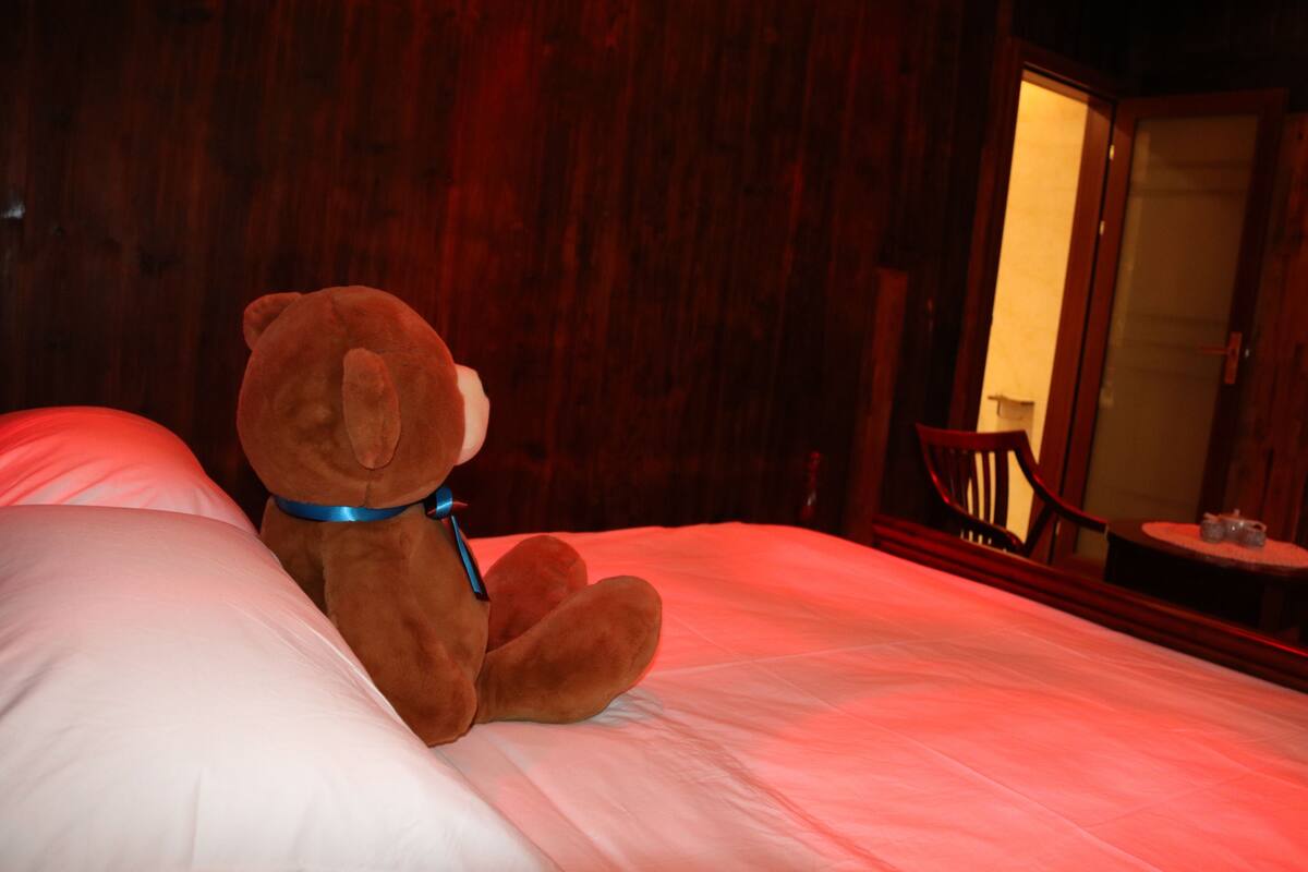 A teddy bear sitting on a bed with a blue collar.