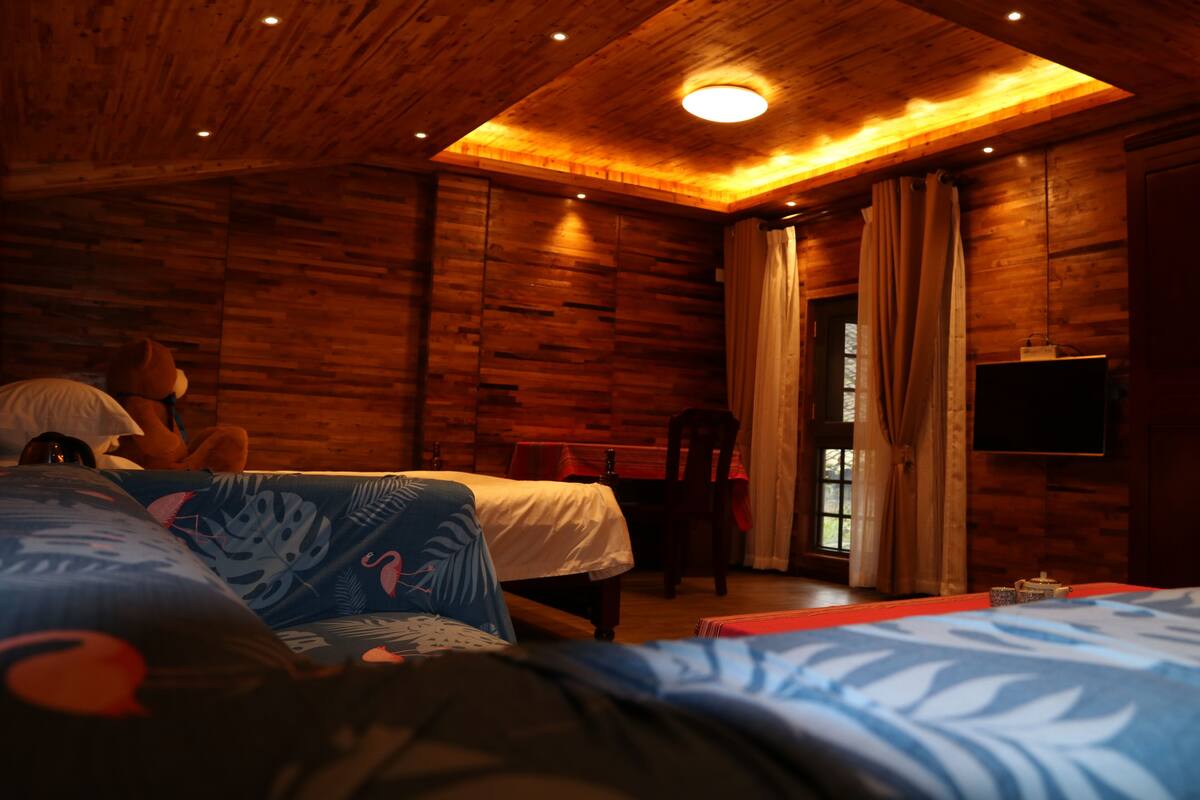 A wooden cabin room with two beds, a TV, and a window with curtains.