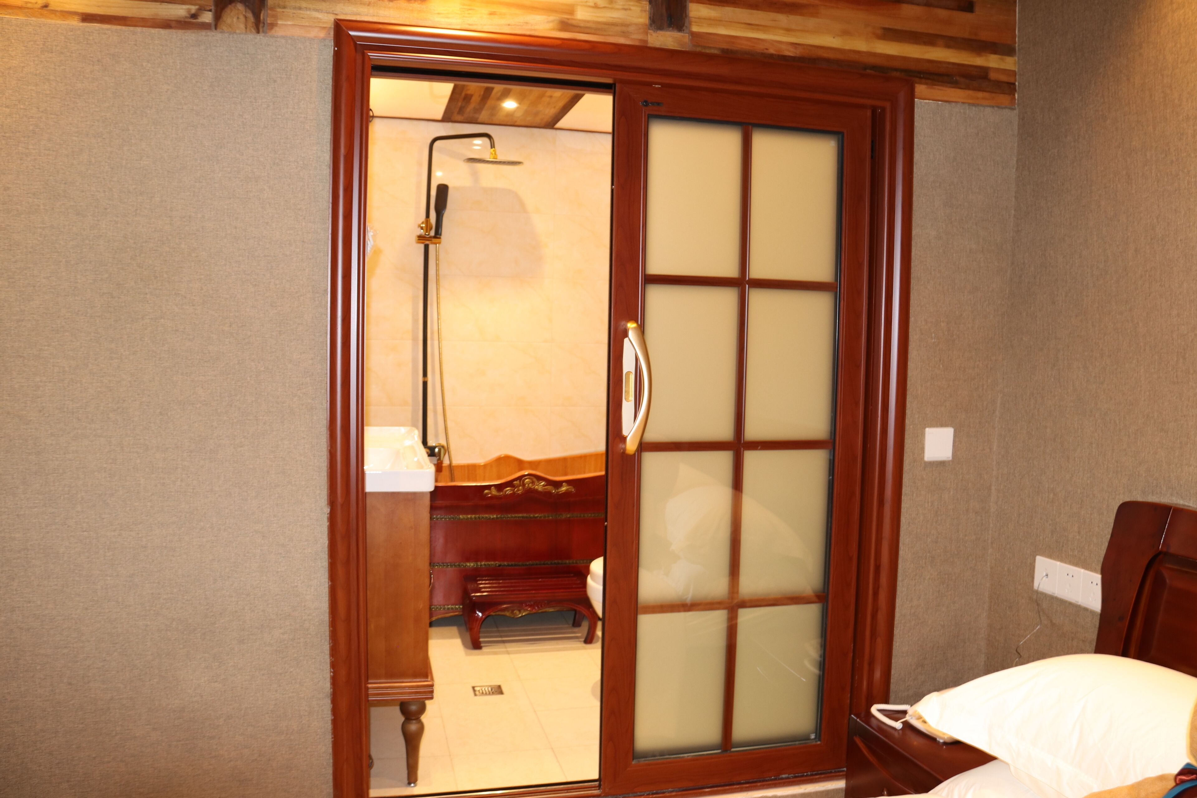 A room with a sliding door leading to a bathroom, a bed with a white pillow, and a wooden bench.