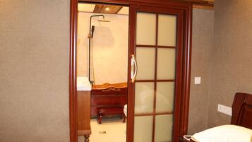 A room with a sliding door leading to a bathroom, a bed with a white pillow, and a wooden bench.