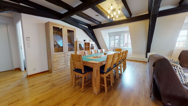 Een eethoek met een houten tafel en stoelen, een kast met glazen deuren en uitzicht buiten door grote ramen.