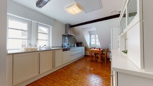 Een keuken met een groot raam, een fornuis, en een eethoek met stoelen en een tafel.