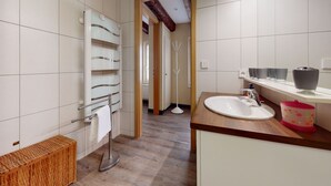 Een moderne badkamer met een houten vloer, witte betegelde wanden, een wit wastafelmeubel en een douchehoek.