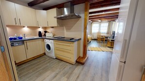 Een compacte keuken met houten kastjes, een ingebouwde wasmachine en een eethoek met tafel en stoelen.