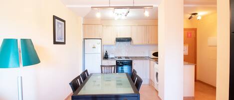 A compact kitchen with a dining area, a washing machine, and a refrigerator.