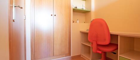 Una habitación con un armario de madera, un escritorio con una silla roja y cajones verdes.
