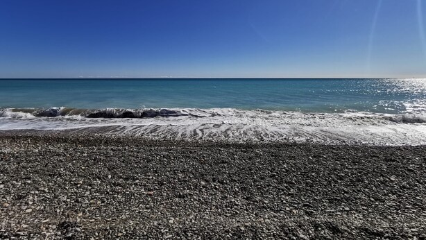 Ein Strand mit Kiesstrand und ruhigem Meer unter blauem Himmel.