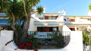Un edificio de dos pisos con fachada blanca, balcones y una pared blanca curva adornada con flores rojas.
