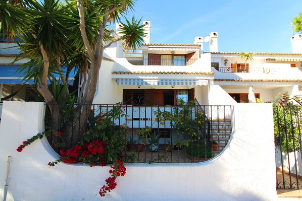 A two-story building with a white facade, balconies, and a curved white wall with red flowers.