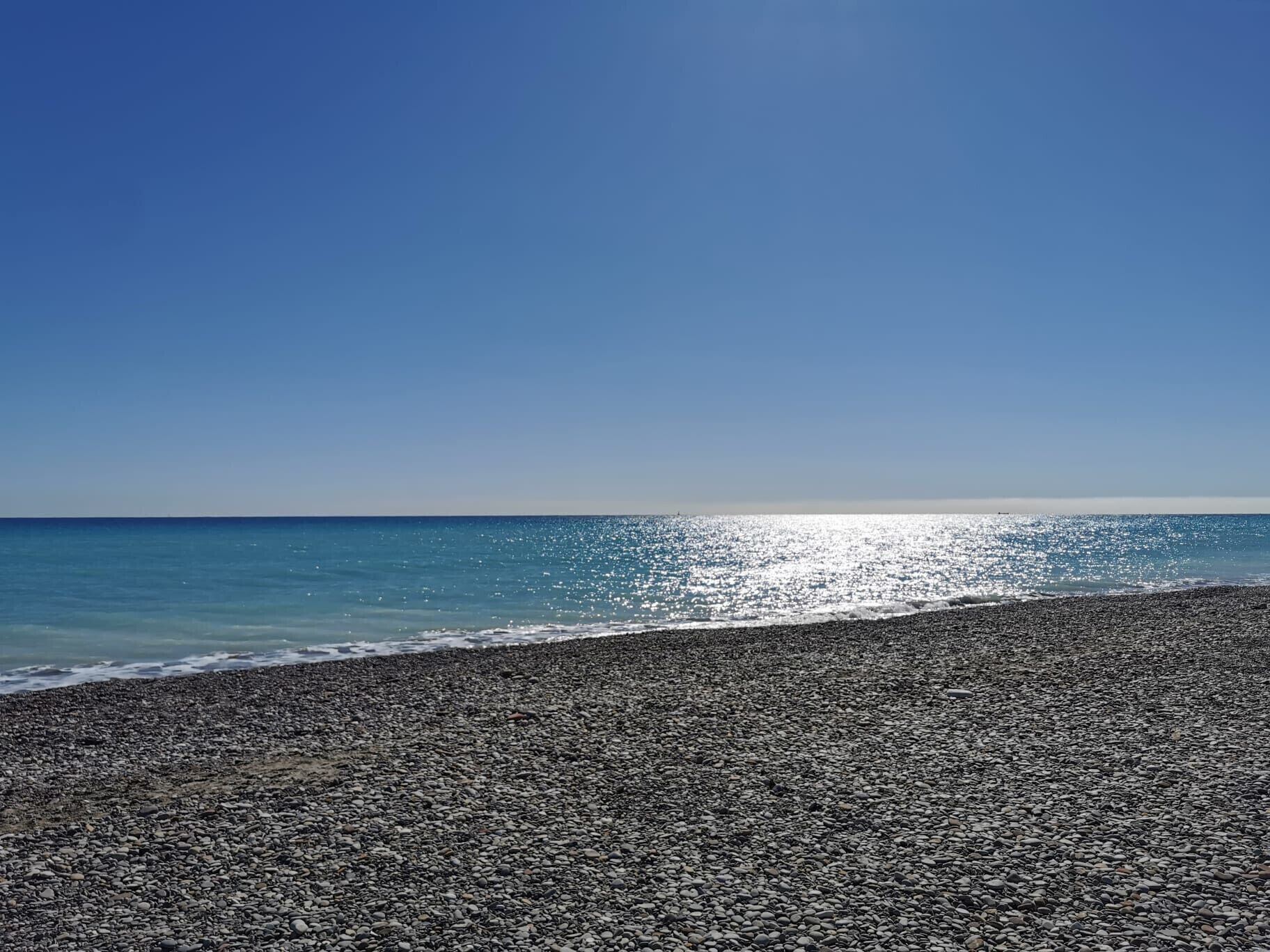 Une plage de galets, avec un ciel dégagé et une mer calme.