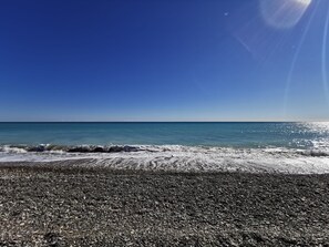 Una playa con orilla de guijarros y mar tranquilo bajo un cielo despejado.