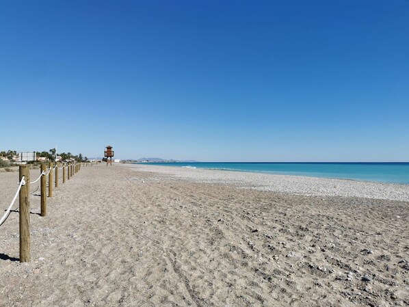 Una playa con una torre de salvavidas, una cerca de madera y un cielo azul despejado.