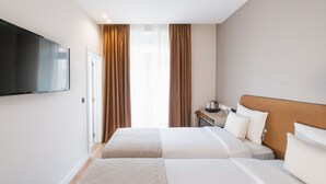 A hotel room with two beds, a TV, a desk with a lamp, and a window with curtains. - Lx SoHo Boutique Hotel by RIDAN Hotels (Lisbon)