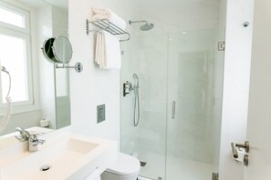 Een moderne badkamer met een glazen douchecabine, een witte wastafel en een spiegel.