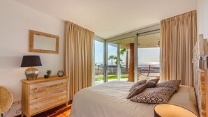 Une chambre avec un grand lit, une commode en bois, une lampe et une vue sur l’extérieur grâce à une porte-fenêtre coulissante.