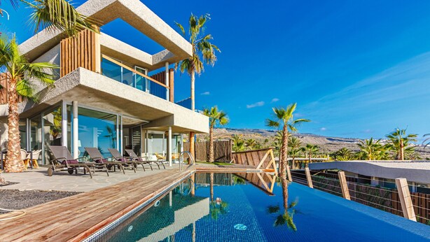 Un hôtel moderne doté d’une grande piscine à débordement, d’une terrasse en bois et de chaises longues.