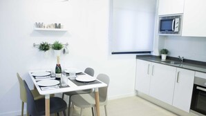 A modern kitchen with white cabinets, a microwave, and a sink. There is a dining table set with plates, glasses, and a bottle of champagne. - IBERICABEDS CENTER 1 BEDROOM (Granada)