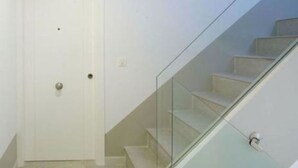 A modern staircase with glass railings leading to a door with a small window above it. - IBERICABEDS CENTER 1 BEDROOM (Granada)