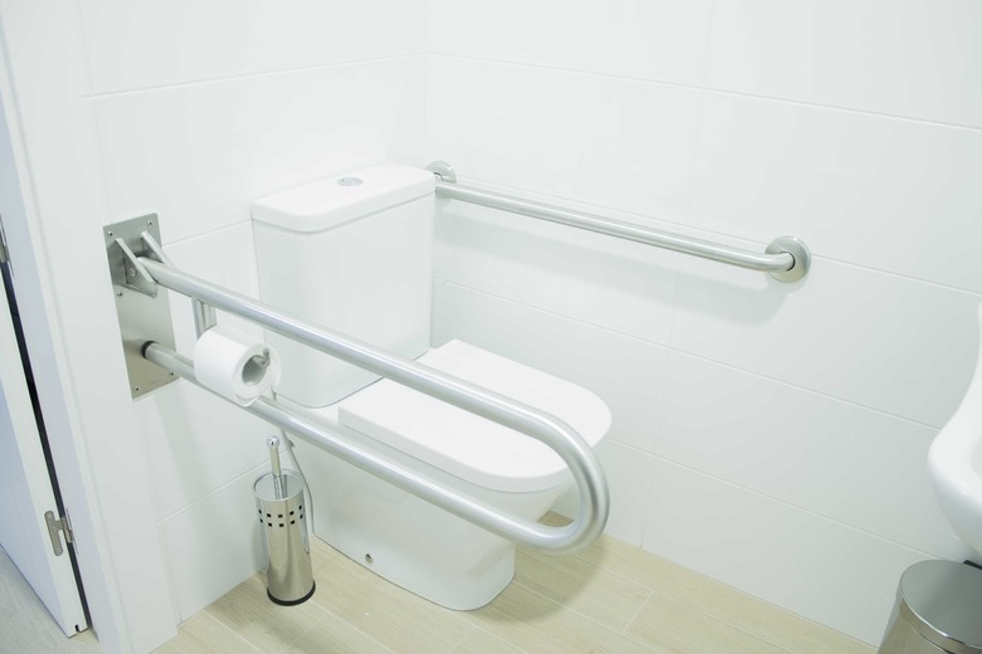 Inodoro blanco con una barra de apoyo a la derecha y un dispensador de papel higiénico a la izquierda.