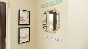 Ein Flur mit gerahmten Kunstwerken, einem Spiegel und Schildern mit der Aufschrift 'The Beach House' und 'Seaside Retreat'.