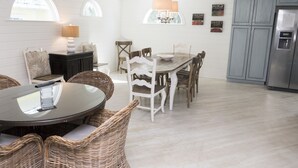 Eine Küche mit Esstisch, Korbstühlen, einer Chandelüster und einem Kühlschrank.