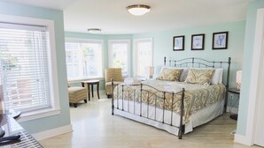 Ein Schlafzimmer mit einem Metallbettgestell, einem Sessel, einem Schreibtisch und einem Fenster mit Jalousien.