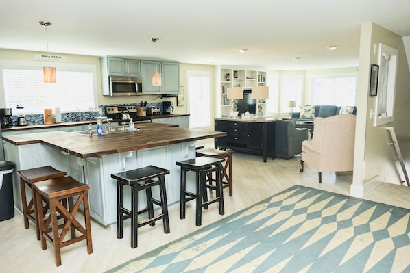 Una cocina moderna con una isla central, taburetes de bar y una zona de comedor con sofá y mesa baja.