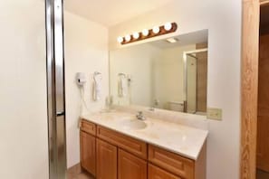 A bathroom with a double sink, wooden cabinets, a large mirror with lights, and a shower door. - 3104 Golf View Hillcrest Ole Bears Cove (Pigeon Forge)