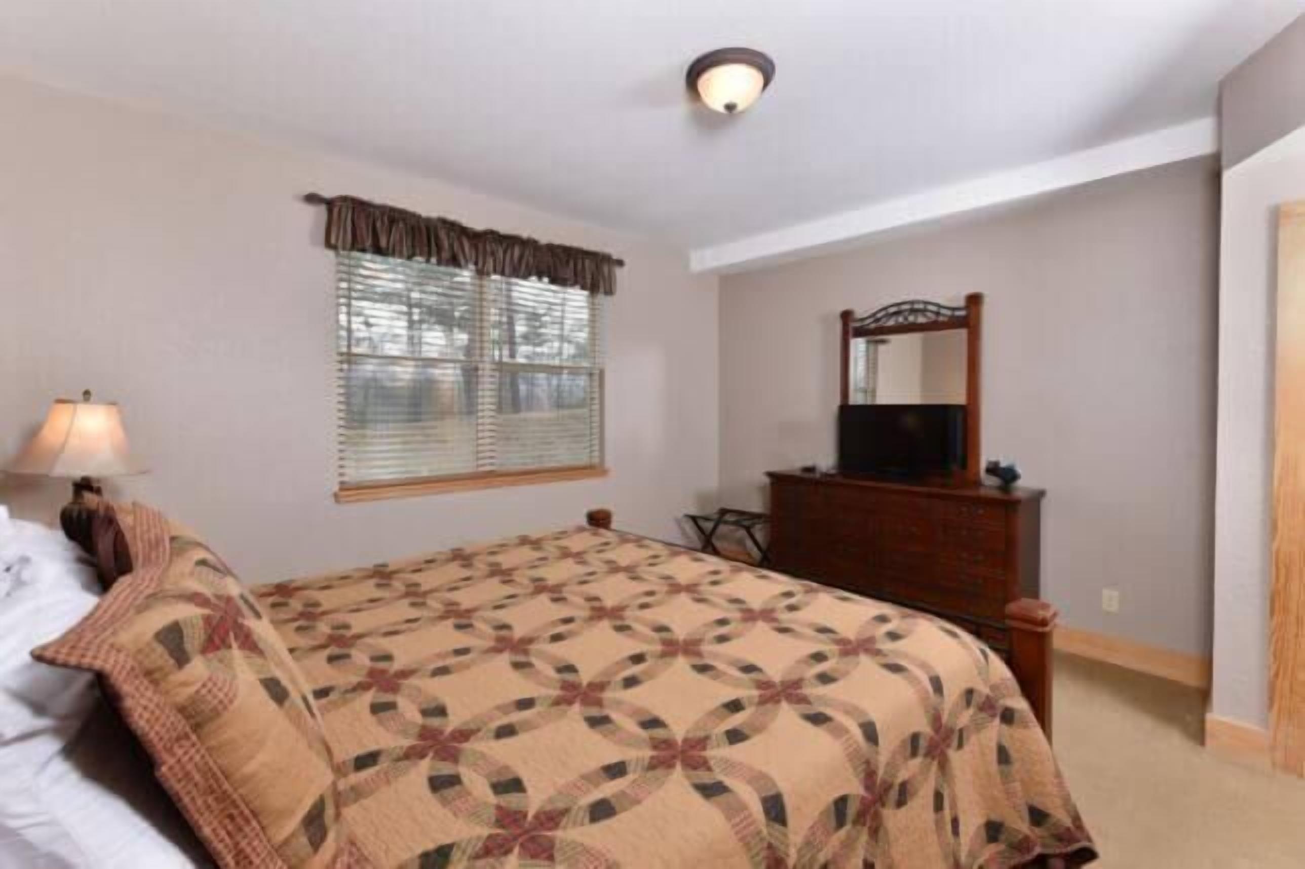 A bedroom with a bed, a dresser, a mirror, and a window with blinds.